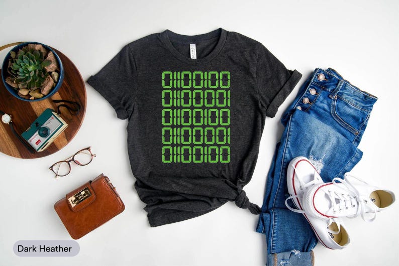 a casual outfit consisting of a black t-shirt with a green digital design, a pair of blue jeans, white sneakers, and a brown wallet. The items are arranged on a white background, creating a visually appealing and organized composition.
