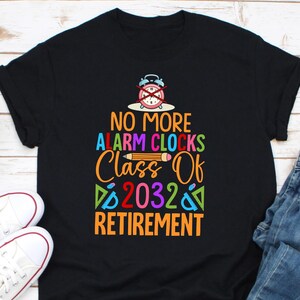 Pode incluir: Camiseta preta com um gráfico colorido que diz "NO MORE ALARM CLOCKS Class Of 2032 Retirement". O design inclui um despertador riscado, um lápis e texto multicolorido. Tênis brancos visíveis no canto inferior esquerdo.