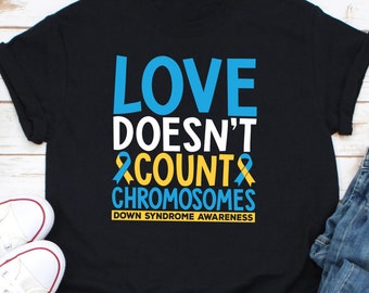 May include: Black t-shirt with the text "LOVE DOESN'T COUNT CHROMOSOMES" in blue and white. The design includes a blue and yellow ribbon, and the words "DOWN SYNDROME AWARENESS" in yellow.