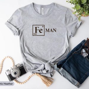 a casual outfit consisting of a gray t-shirt with a chemical element design, a pair of denim shorts, a camera, and a potted plant.