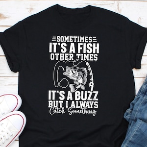 May include: Black t-shirt with white text and a fish graphic. The text reads "Sometimes it's a fish, other times it's a buzz, but I always catch something." A fishing rod and fish are also depicted.