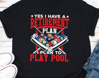 May include: Black t-shirt featuring the text "YES I HAVE A RETIREMENT PLAN I PLAN TO PLAY POOL" in red and white. The design includes a rack of billiard balls and crossed pool cues.