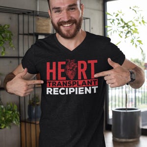 May include: A black V-neck t-shirt with the text "HEART TRANSPLANT RECIPIENT" in red letters. A red anatomical heart graphic is centred above the text.