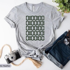 a gray t-shirt with a digital print of a repeating pattern of numbers, a pair of blue jeans, a camera, and a potted plant.