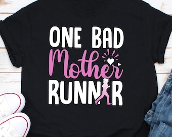 May include: Black t-shirt with white text that reads "One Bad Mother Runner" with a pink silhouette of a running woman and a pink heart.