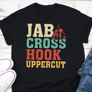 May include: Black t-shirt with a vintage-style graphic that says "JAB CROSS HOOK UPPERCUT" with a pair of red boxing gloves hanging from the top of the text.
