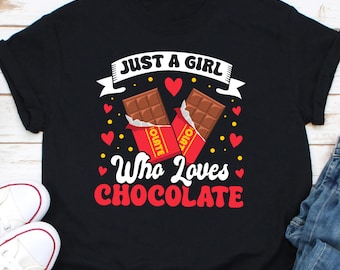 Peut inclure: T-shirt noir avec l'inscription "JUST A GIRL Who Loves CHOCOLATE" en blanc et rouge. Le motif comprend deux barres de chocolat, des cœurs rouges et des points jaunes.