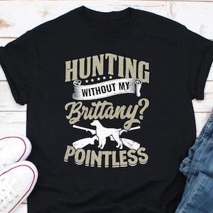 May include: Black t-shirt with a hunting-themed design. The text reads "Hunting Without My Brittany? Pointless". A white Brittany dog is pictured in the center of the design.