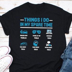 May include: A black t-shirt with a blue graphic that says "Things I do in my spare time" and lists activities related to Tesla cars. The activities include washing, staring at, researching, talking about, thinking about, and dreaming about Tesla.
