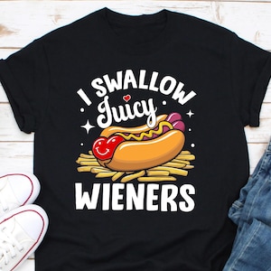 May include: Black t-shirt with a white graphic of a hot dog with mustard and ketchup, and the text "I Swallow Juicy Wieners".