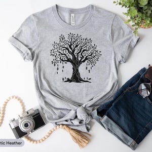 a casual outfit consisting of a gray t-shirt with a tree graphic, a pair of blue jeans, a pair of sunglasses, a camera, and some beads.