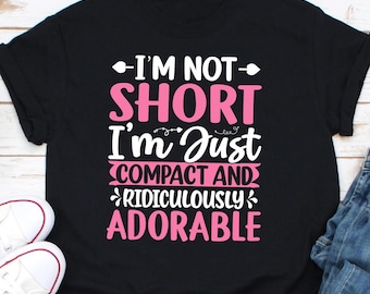 Puede incluir: Camiseta negra con texto blanco que dice "No soy baja, solo soy compacta y ridículamente adorable" en letras rosas.