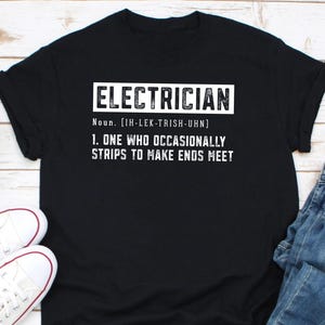 May include: Black t-shirt with white text that reads "ELECTRICIAN Noun. [IH-LEK-TRISH-UHN] 1. ONE WHO OCCASIONALLY STRIPS TO MAKE ENDS MEET"