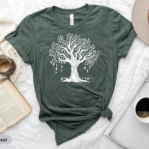a green t-shirt with a white tree graphic, a hat, a book, a cup of coffee, and a clock, all arranged on a white surface.