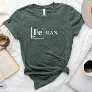 a green t-shirt with a white text design, a hat, a book, a cup of coffee, and a clock, all arranged on a white surface.