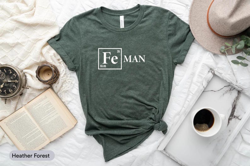 a green t-shirt with a white text design, a hat, a book, a cup of coffee, and a clock, all arranged on a white surface.