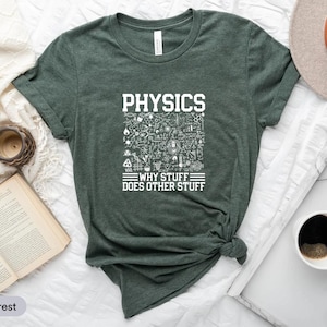 Puede incluir: Camiseta verde bosque jaspeado con la palabra "PHYSICS" en letras blancas. Debajo, un gráfico de garabatos científicos y la frase "WHY STUFF DOES OTHER STUFF". La camiseta se muestra sobre una superficie blanca.