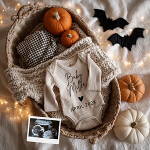 May include: A beige baby onesie with the text "Baby Miller" and "APRIL 202X" is in a woven basket with pumpkins, a blanket, and a black and white checkered cloth. Two black bat cutouts and a sonogram photo complete the autumn-themed arrangement.