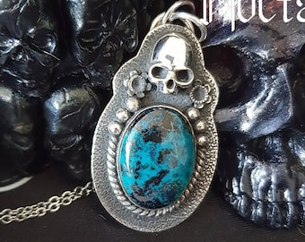 Puede incluir: Un colgante de plata con una piedra turquesa y un diseño de calavera. El colgante está en una cadena de plata y está rodeado de calaveras negras. El texto "LA COLLECTION" y "Mocta" es visible en la imagen. El sitio web "www.atelierkorrigane.com" también es visible.