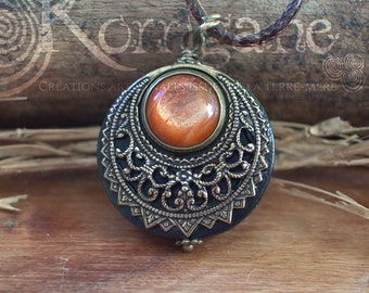 May include: A round pendant necklace with an orange sunstone cabochon set in a brass filigree frame. The pendant is hanging on a brown cord.
