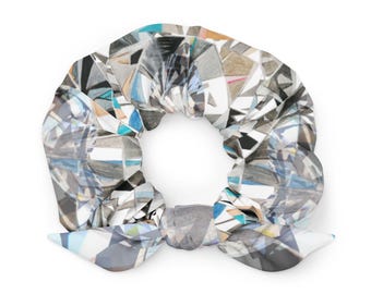 May include: A scrunchie featuring a geometric diamond design in grey, white, blue, and tan. The fabric is gathered and tied into a bow shape. This hair accessory adds a touch of elegance to any hairstyle.