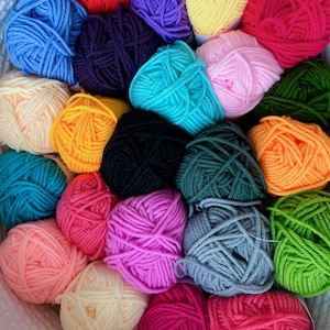 May include: A collection of colorful yarn balls in various shades of blue, green, red, pink, orange, yellow, and black. The yarn is arranged in a circular pattern, creating a visually appealing display.