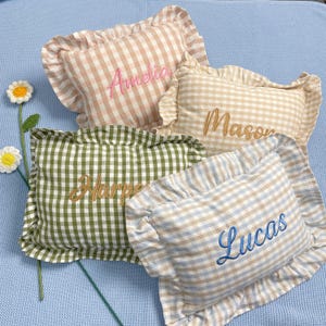 May include: Four gingham-patterned pillows in pink, beige, green, and blue. Each pillow has an embroidered name: Amelia, Mason, Harper, and Lucas. The pillows have ruffled edges.