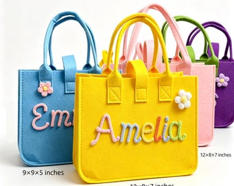 May include: A collection of felt tote bags in blue, yellow, pink, green, and purple. Each bag features a name in raised, colorful rope lettering and a small crocheted flower. Dimensions are labeled as 9x9x5 inches and 12x8x7 inches.