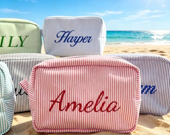 May include: A collection of rectangular zippered pouches made of striped fabric in various colors including red, blue, and green. Each pouch features a personalized name embroidered on the front, such as Amelia, Harper, and Lily, in script font.