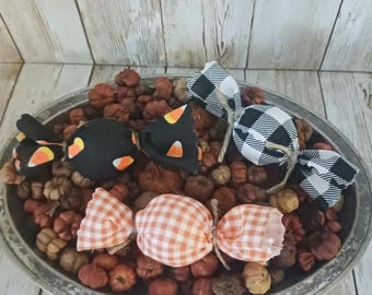 May include: A decorative arrangement featuring fabric candy decorations in a metal tray filled with small pumpkins. The candy shapes are black, orange gingham, and black and white buffalo check, with candy corn accents. A rustic fall theme.