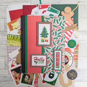 May include: A collection of Christmas-themed stationery and decorations. Includes a red and green journal with a Christmas tree graphic, gift tags, stickers, and cards with holiday greetings. The color palette is dominated by red, green, and white.