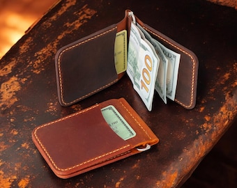 May include: A brown leather wallet with a money clip and a separate card slot. The wallet is open and has several bills inside.