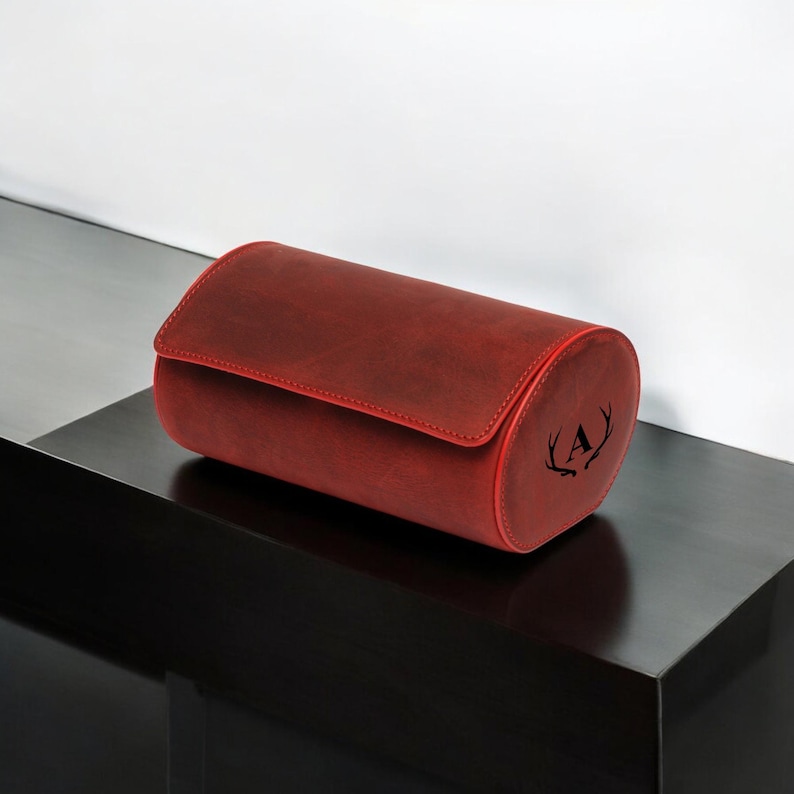 May include: A red leather watch winder with a monogrammed initial "A" and antlers on the side.