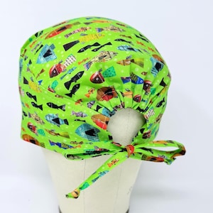 May include: A lime green scrub cap with a colorful fish pattern. The cap features a tie closure and is displayed on a mannequin head. The fish are in various colors, including blue, red, and yellow.