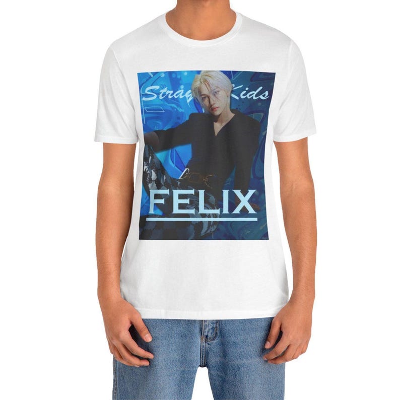 Male model showcasing the unisex, 100% airlume combed & ring-spun cotton t-shirt in white, featuring a graphic design. It shows Felix from Stray Kids in a provocative pose, wearing a structured black suit jacket and oriental-style patterned pants. The background is a multi-toned blue graffiti. From ModeK Vetements.