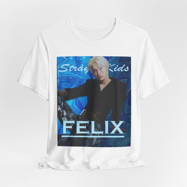 Draped unisex, 100% airlume combed & ring-spun cotton t-shirt in white, featuring a graphic design. It shows Felix from Stray Kids in a provocative pose, wearing a structured black suit jacket and oriental-style patterned pants. The background is a multi-toned blue graffiti. From ModeK Vetements.