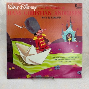 May include: A vintage Walt Disney record album cover featuring "The Stories of Hans Christian Andersen." The cover art depicts a toy soldier, a paper boat, and a castle. The album is titled "The Steadfast Tin Soldier, The Little Match Girl and Others."