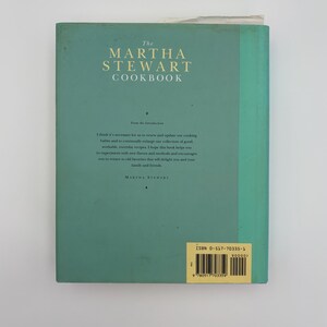 Puede incluir: La contraportada turquesa de "The Martha Stewart Cookbook" con texto blanco. El t&iacute;tulo est&aacute; en la parte superior, con una introducci&oacute;n debajo. El ISBN est&aacute; en una etiqueta amarilla. Un libro de cocina cl&aacute;sico.