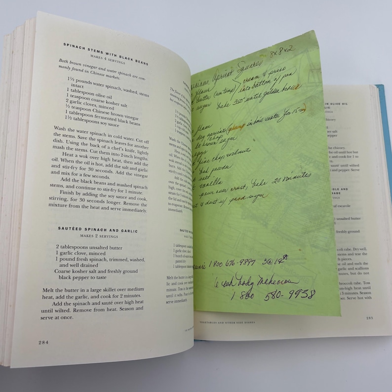 Puede incluir: P&aacute;ginas de libro de cocina abiertas con recetas de espinacas. Una nota adhesiva verde con una receta manuscrita est&aacute; insertada. El libro est&aacute; sobre una superficie blanca.