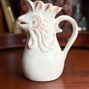 May include: A white ceramic mug with a black handle and the text "But First, Coffee" in a black, bold font. The mug is on a white surface.