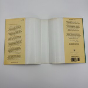 Puede incluir: Libro de cocina abierto con una cubierta de color amarillo claro y lomo verde. El libro est&aacute; abierto en una p&aacute;gina en blanco. El texto de la portada incluye "The Martha Stewart Cookbook" y otro texto. El libro est&aacute; sobre una superficie blanca.
