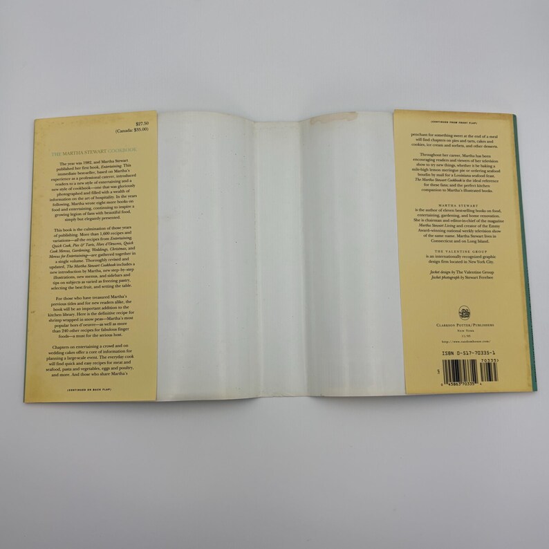 Puede incluir: Libro de cocina abierto con una cubierta de color amarillo claro y lomo verde. El libro est&aacute; abierto en una p&aacute;gina en blanco. El texto de la portada incluye "The Martha Stewart Cookbook" y otro texto. El libro est&aacute; sobre una superficie blanca.