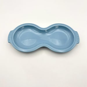 May include: A light blue, peanut-shaped serving dish with two rounded, concave sections. The dish features a smooth, glossy finish and small, integrated handles on each end with a subtle, vertical ribbed texture along the outer edges.