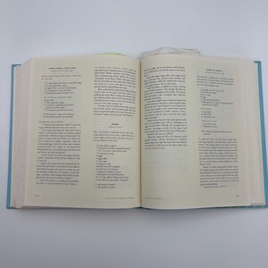 Puede incluir: Un libro de cocina abierto con cubiertas azul claro, que muestra recetas en p&aacute;ginas de color crema. La p&aacute;gina izquierda presenta una receta de "Lemon Angel Food Cake", mientras que la p&aacute;gina derecha tiene una receta titulada "To Make the Lemon Curd". El libro est&aacute; abierto sobre una superficie blanca.