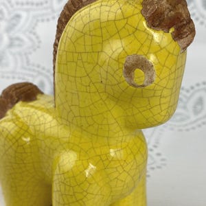 May include: A ceramic horse figurine with a yellow crackle glaze and brown mane and tail. The horse has a stylized, geometric design and is standing on four legs. The figurine is a decorative item.