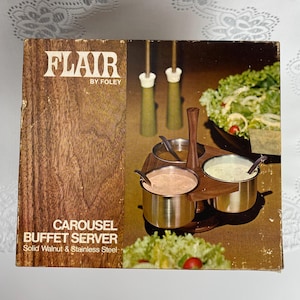 May include: A vintage "Flair" carousel buffet server in its original box. The box features the text "Flair by Foley" and "Carousel Buffet Server Solid Walnut & Stainless Steel". The server includes three stainless steel bowls with spoons, set in a wooden carousel.
