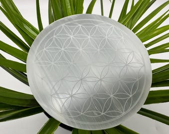 May include: A white selenite charging plate with a flower of life design etched into the surface. The plate is round and has a smooth, polished finish.