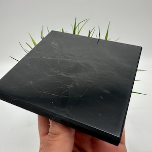 May include: A black square slate tile with a smooth, polished surface. The tile has a subtle marbled pattern and is perfect for displaying small objects.