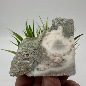 Puede incluir: Una piedra natural rugosa con un patrón blanco y verde. La piedra tiene una superficie lisa y pulida y es de color verde claro con remolinos blancos.