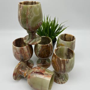 May include: Set of six green and brown marble drinking glasses with a stemmed base. The glasses are stacked on top of each other.